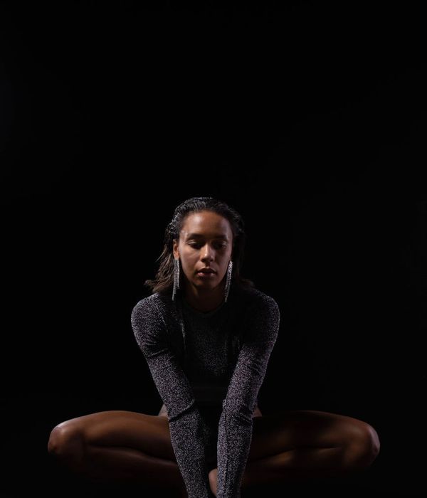 Woman in a calm yoga pose, embodying balance and grace in a dark studio.